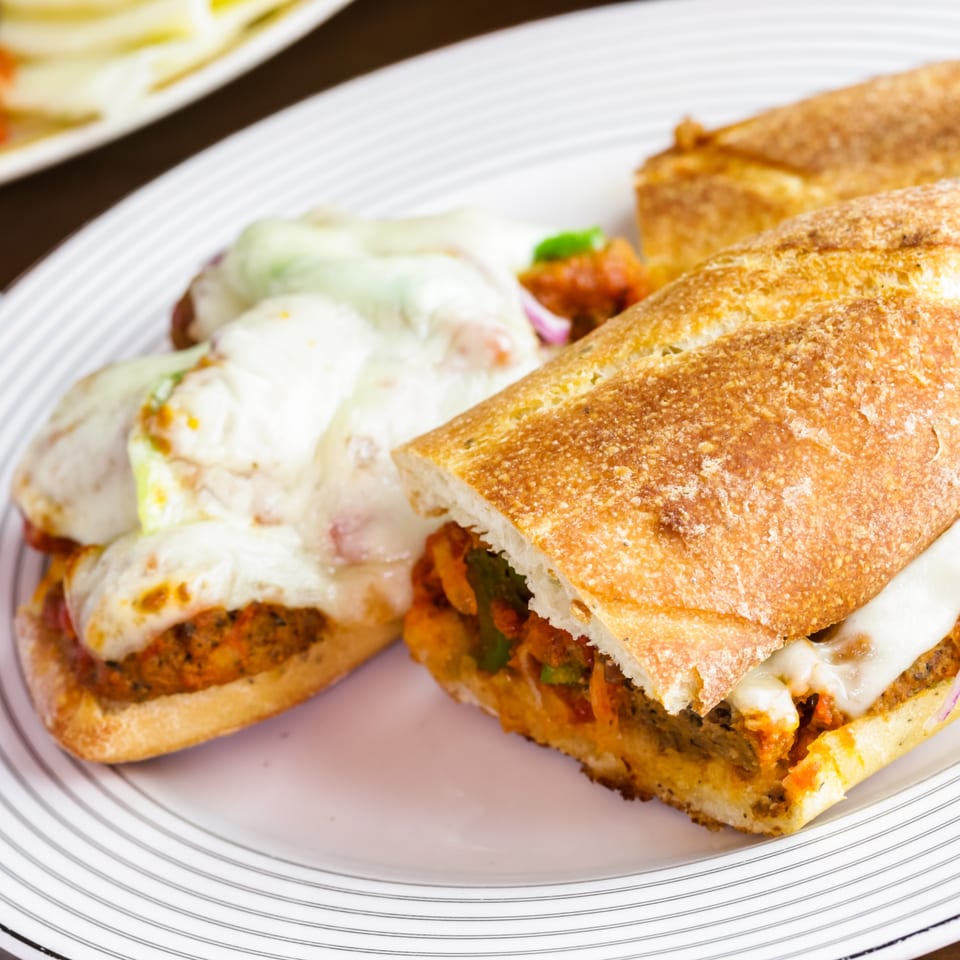 Two halves of a Deli Counter Sandwich Shop meatball sub, topped with melted cheese, on a white plate.