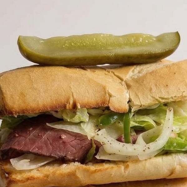 A submarine sandwich with roast beef, lettuce, onions, and green peppers, topped with a pickle spear.