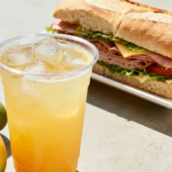 Iced tea with lemon and a large deli sandwich on a baguette with meat, cheese, and lettuce.